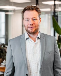 Man in gray blazer in the office smiling at the camera