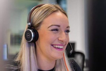 Customer service representative with headset smiling at her computer screen