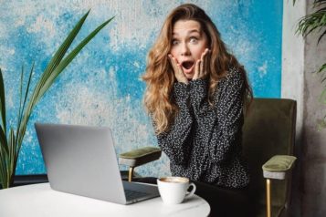 Woman sitting behind laptop with a shocked face looking at the camera